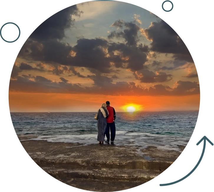 Two people standing on a beach at sunset.