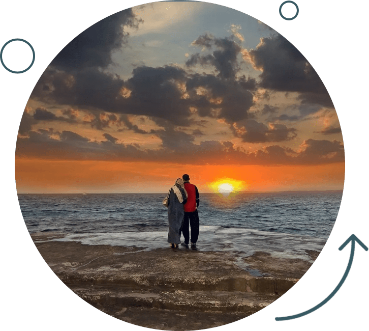 Two people standing on a beach at sunset.